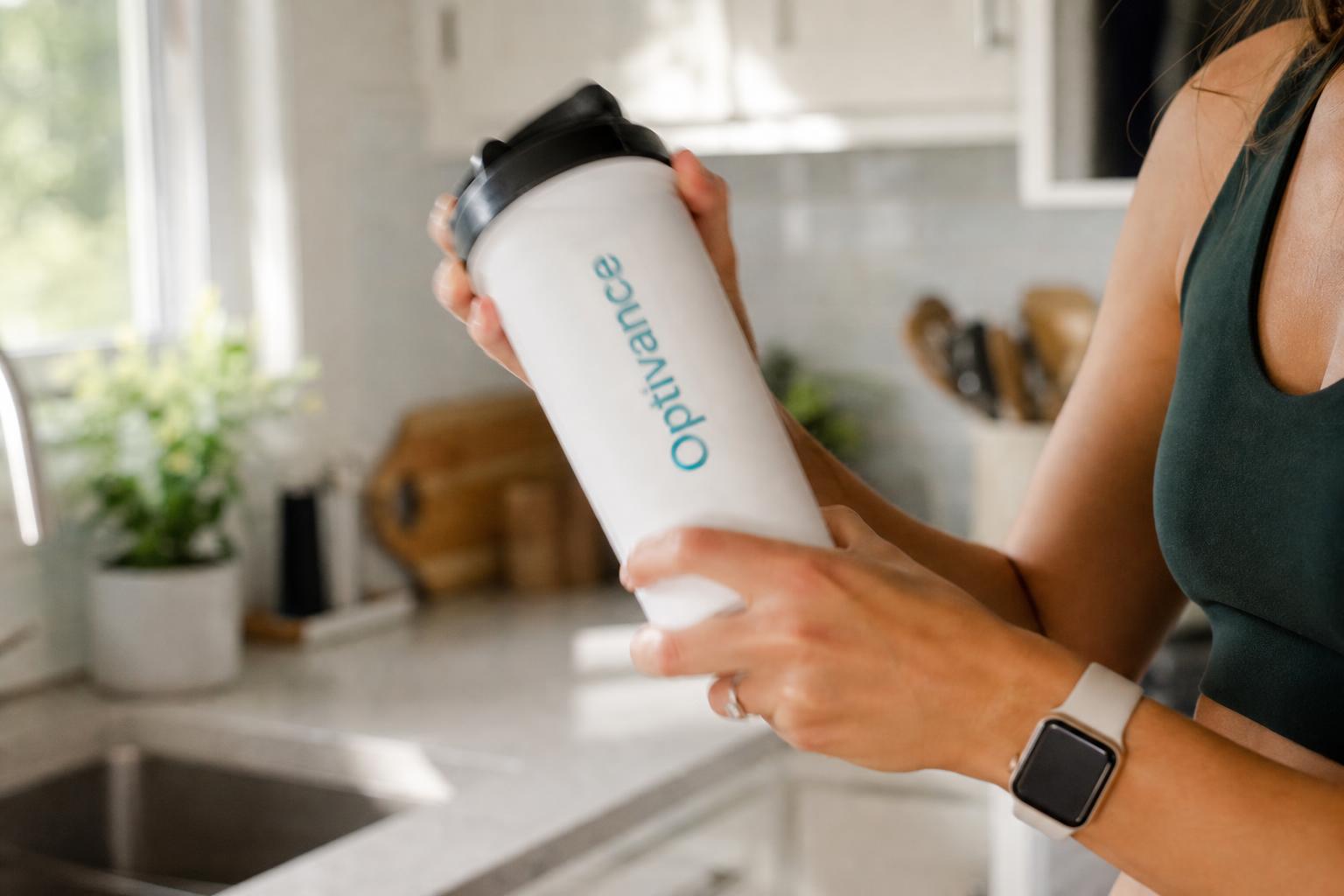 Woman shaking the official Optivance shaker bottle in a bright kitchen.